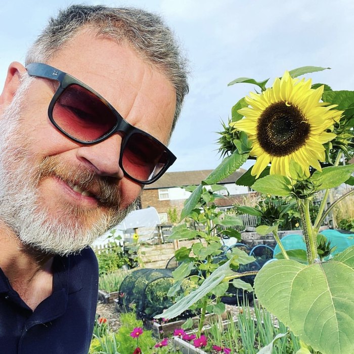 Tony Smith on his plot, next to a sunflower taller than he is